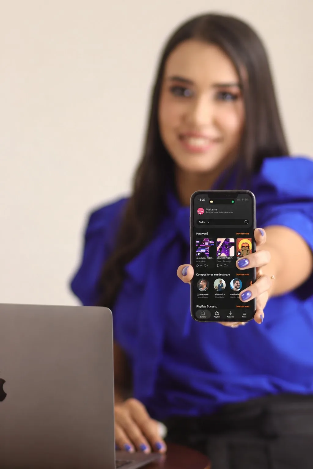 Rafaella Santos segurando um celular com um app aberto, ao lado de um notebook